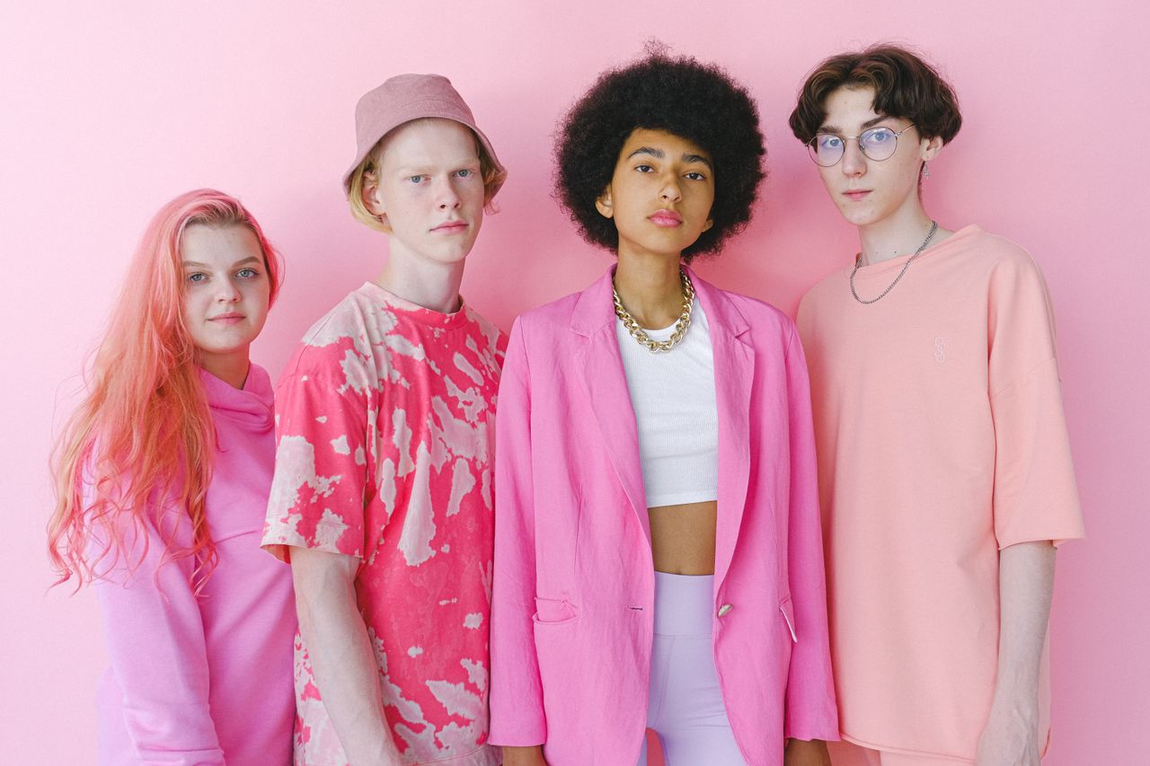 Diverse teenage friends in trendy outfits looking at camera on pink background of studio